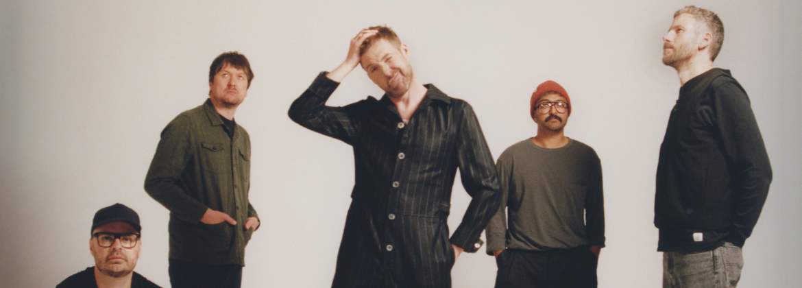 Five men posing in different stances in front of a white wall