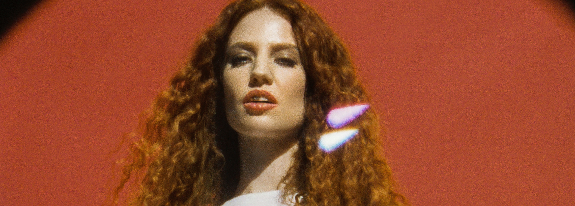 A woman with curly hair staring at the camera wearing lip gloss, with a red background