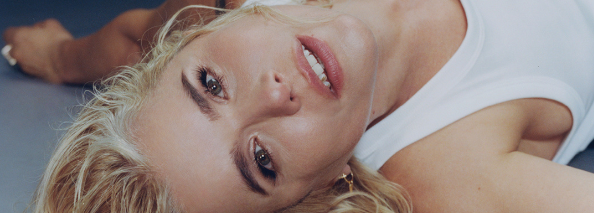 A woman laying down wearing a white tank top looking at the camera smiling