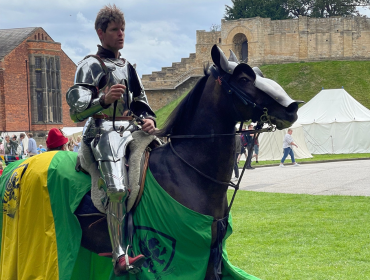 A medieval knight in armour on horseback in the castle grounds