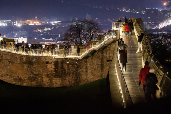 Illuminated medieval wall walk in the evening with people walking along